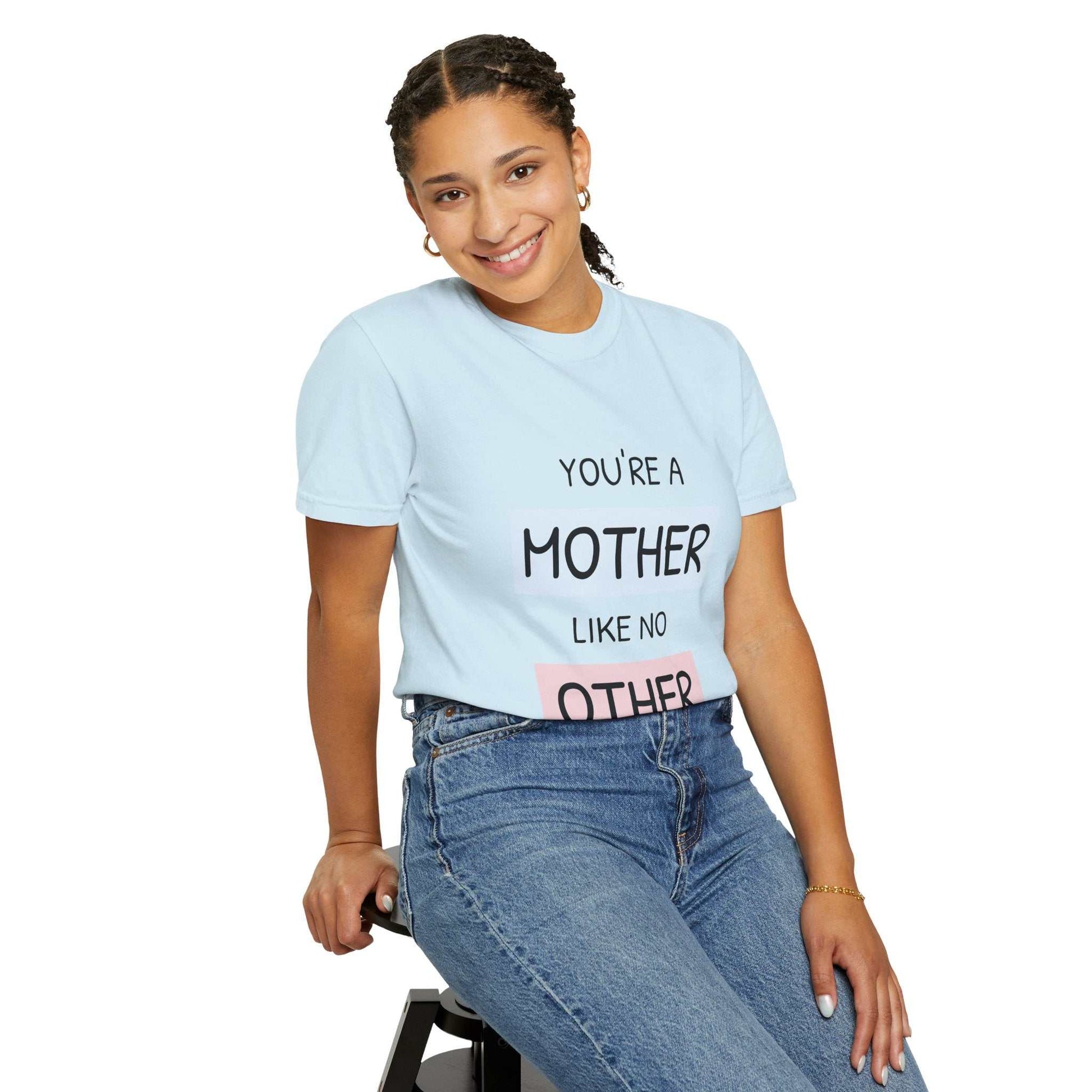 Woman wearing "You're a Mother Like No Other" T-shirt with blue relaxed fit, sitting and smiling, celebrating unique motherhood bond.